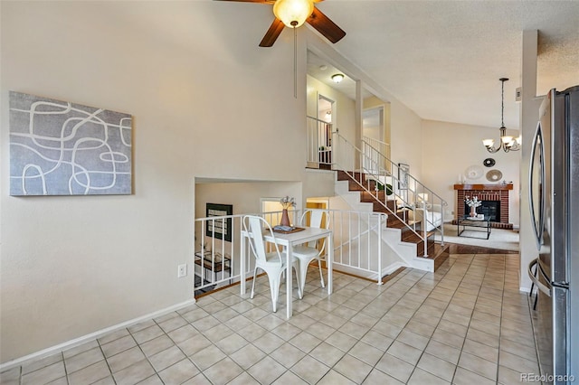 entryway featuring stairway, light tile patterned floors, ceiling fan with notable chandelier, and a brick fireplace