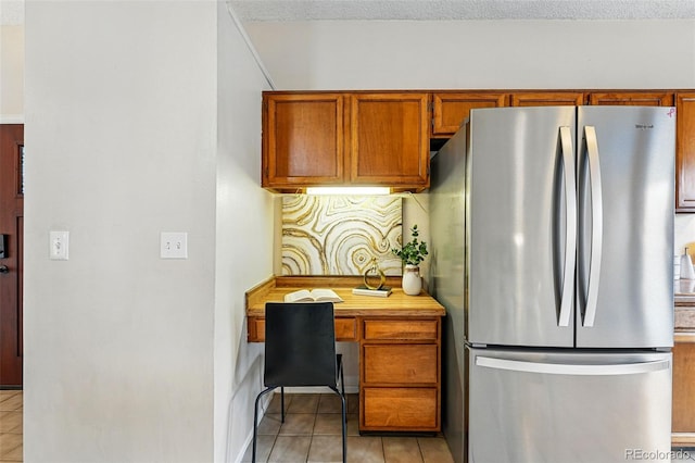 kitchen featuring freestanding refrigerator, brown cabinets, light tile patterned floors, and built in study area