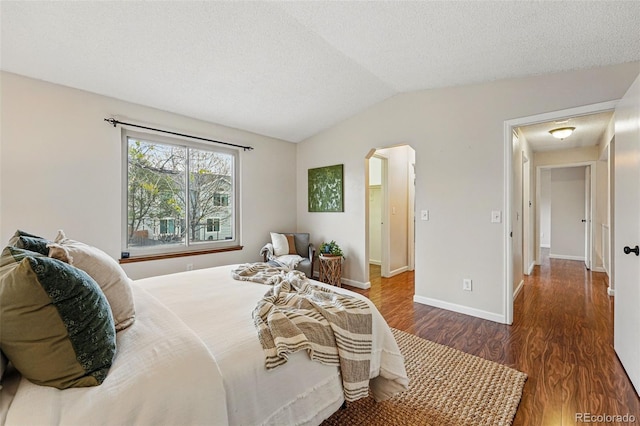 bedroom with wood finished floors, baseboards, a textured ceiling, arched walkways, and vaulted ceiling