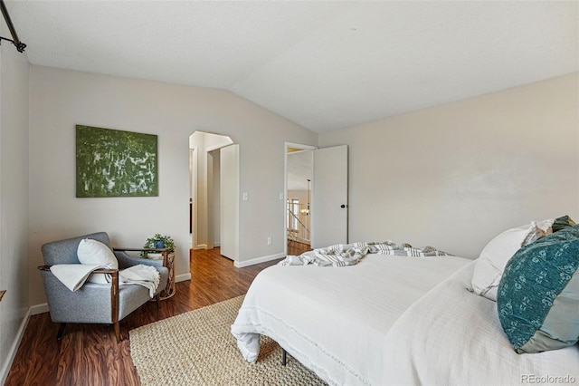 bedroom featuring baseboards, arched walkways, wood finished floors, and lofted ceiling