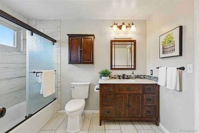 bathroom featuring vanity, baseboards, toilet, and shower / bath combination with glass door