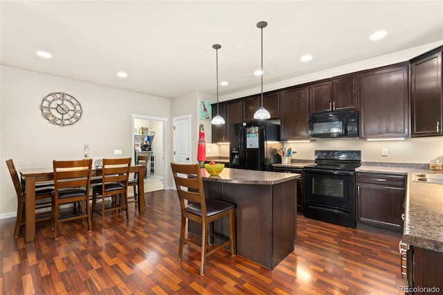 kitchen featuring dark hardwood / wood-style floors, pendant lighting, a kitchen bar, a kitchen island, and black appliances