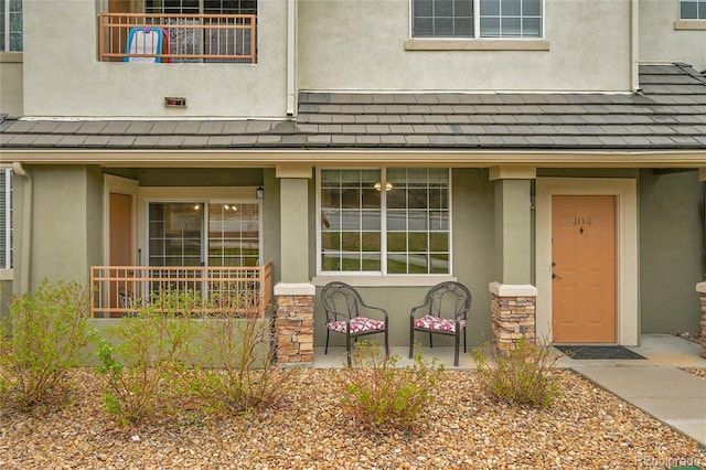 view of exterior entry with stucco siding, a balcony, stone siding, and covered porch