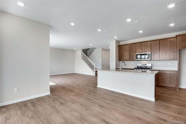 kitchen with range, light wood-type flooring, backsplash, an island with sink, and sink