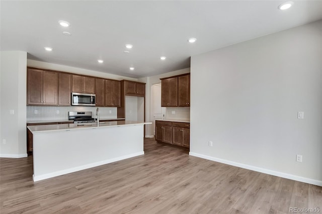 kitchen with stove, tasteful backsplash, a center island with sink, sink, and light wood-type flooring