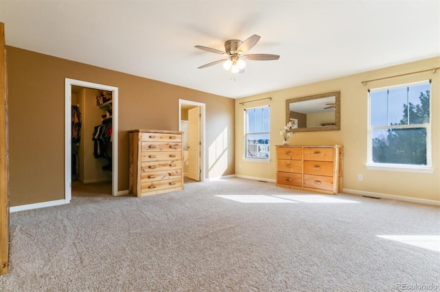 unfurnished bedroom featuring multiple windows, a spacious closet, light carpet, and ceiling fan