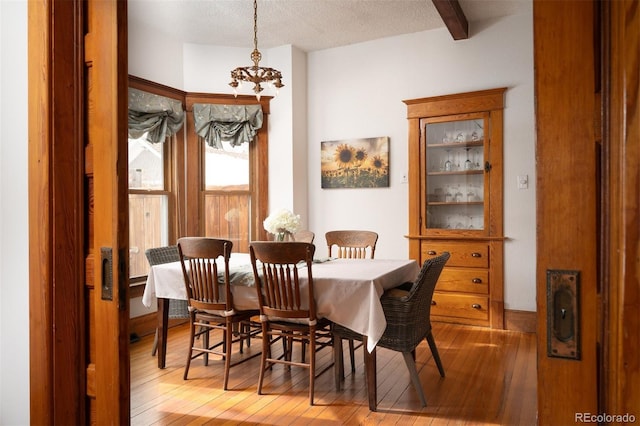 dining area with beam ceiling, a textured ceiling, light hardwood / wood-style flooring, and a chandelier