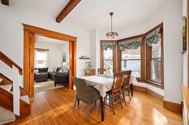 dining room featuring an inviting chandelier, beamed ceiling, a textured ceiling, and light wood-type flooring