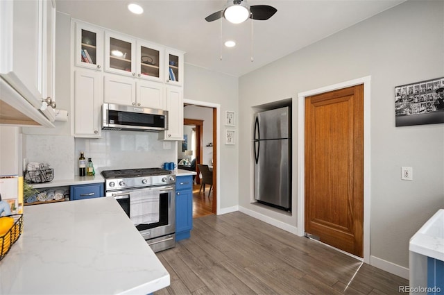 kitchen with appliances with stainless steel finishes, hardwood / wood-style floors, light stone counters, white cabinets, and blue cabinets