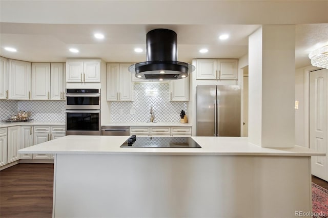 kitchen with tasteful backsplash, dark wood-style floors, island exhaust hood, stainless steel appliances, and light countertops