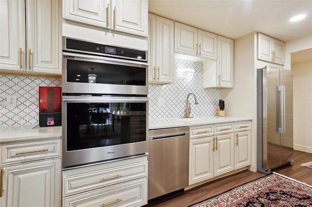 kitchen with appliances with stainless steel finishes, dark wood-style flooring, a sink, and tasteful backsplash