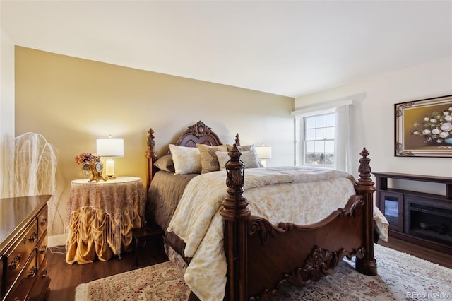 bedroom with a glass covered fireplace and wood finished floors