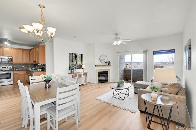 dining room featuring baseboards, a fireplace, light wood-style flooring, and ceiling fan with notable chandelier