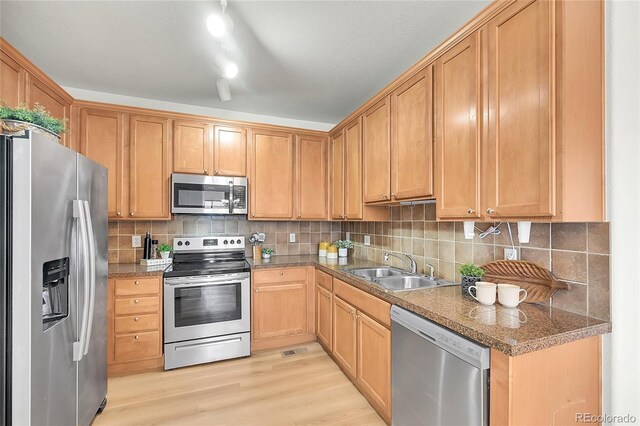 kitchen with tile counters, tasteful backsplash, a sink, light wood-style flooring, and appliances with stainless steel finishes