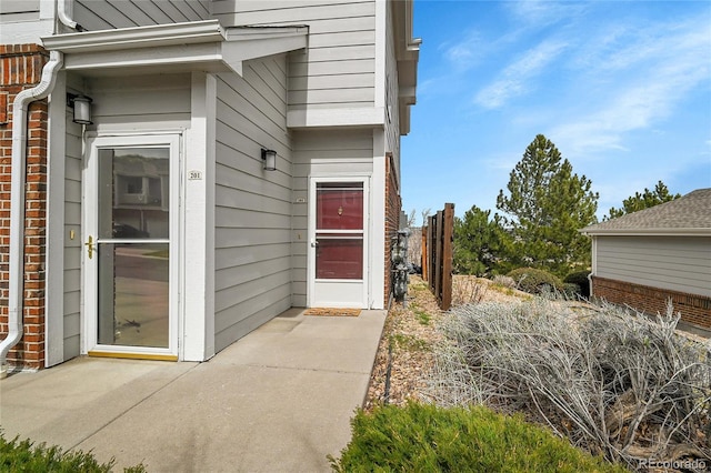 doorway to property featuring fence and brick siding