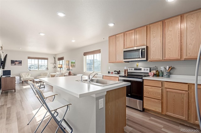 kitchen with sink, appliances with stainless steel finishes, light hardwood / wood-style floors, an island with sink, and light brown cabinetry