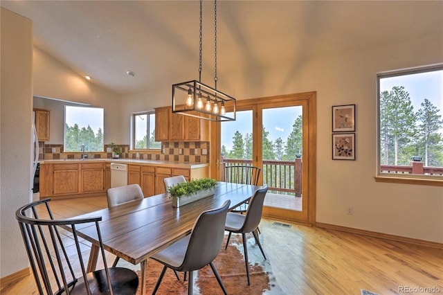 dining space featuring an inviting chandelier, sink, light hardwood / wood-style floors, and vaulted ceiling