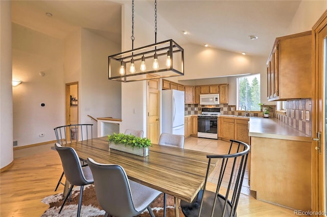 dining room featuring high vaulted ceiling, sink, and light hardwood / wood-style floors