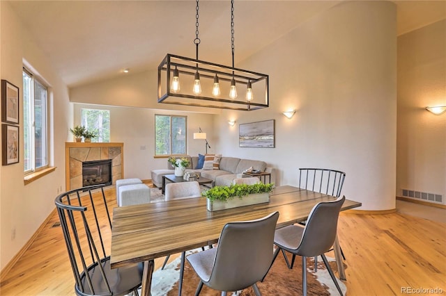 dining room with a tile fireplace, vaulted ceiling, and light wood-type flooring