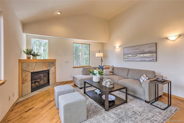 living room featuring a tiled fireplace, high vaulted ceiling, and light hardwood / wood-style flooring