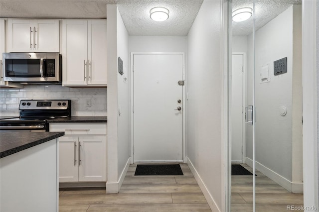 kitchen with appliances with stainless steel finishes, light wood-type flooring, white cabinetry, and decorative backsplash