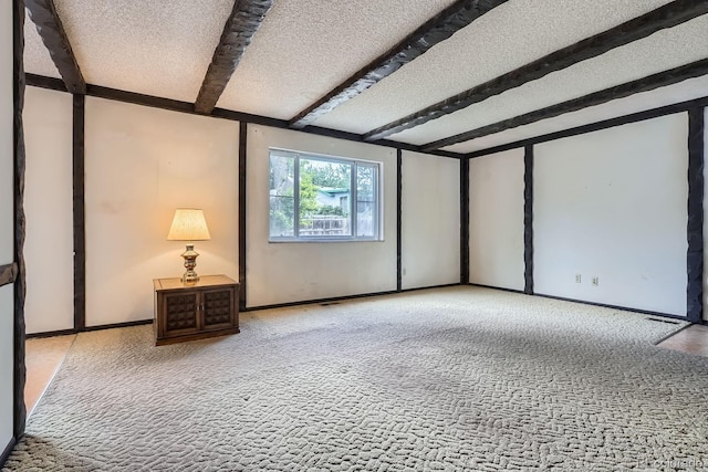 spare room featuring carpet floors, a textured ceiling, beamed ceiling, and baseboards