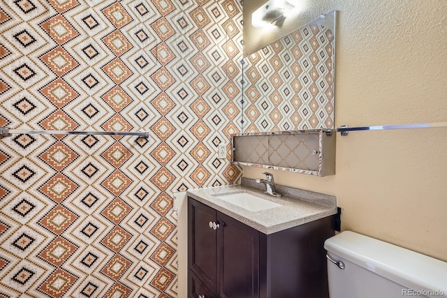bathroom featuring toilet, a textured wall, and vanity
