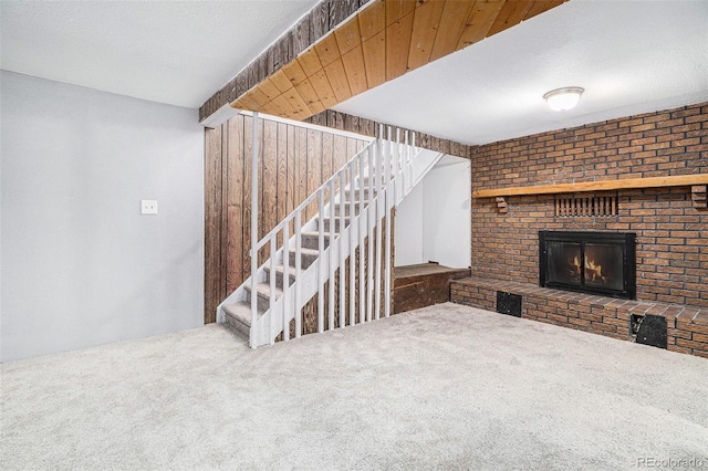 unfurnished living room featuring carpet flooring, a textured ceiling, and a brick fireplace