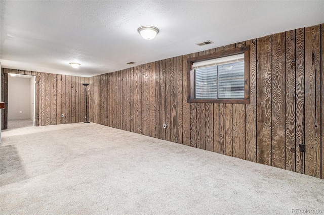 basement featuring wooden walls, carpet floors, and a textured ceiling