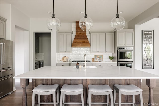 27653 E Euclid Dr, Aurora, CO 80016 - kitchen featuring stainless steel appliances, custom exhaust hood, backsplash, dark wood-style floors, and a kitchen island with sink