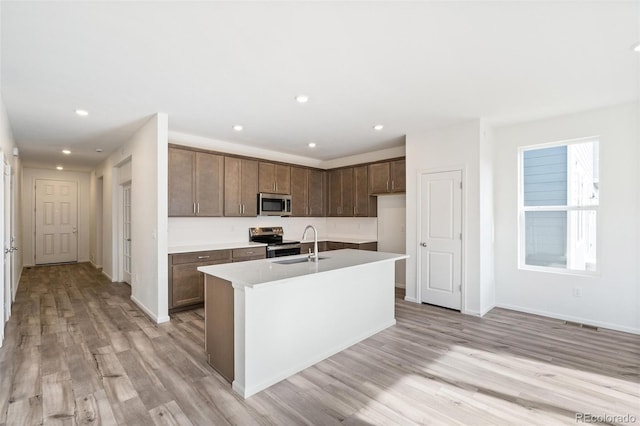 kitchen with light wood-type flooring, sink, a center island with sink, and appliances with stainless steel finishes