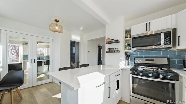 kitchen with white cabinets, hanging light fixtures, kitchen peninsula, stainless steel appliances, and french doors