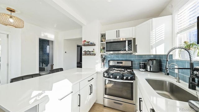 kitchen with stainless steel appliances, kitchen peninsula, sink, and white cabinets