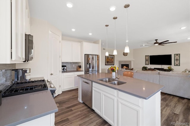 16341 Clayton St, Thornton, CO 80602 - kitchen with appliances with stainless steel finishes, a lit fireplace, backsplash, open floor plan, and dark wood-style flooring
