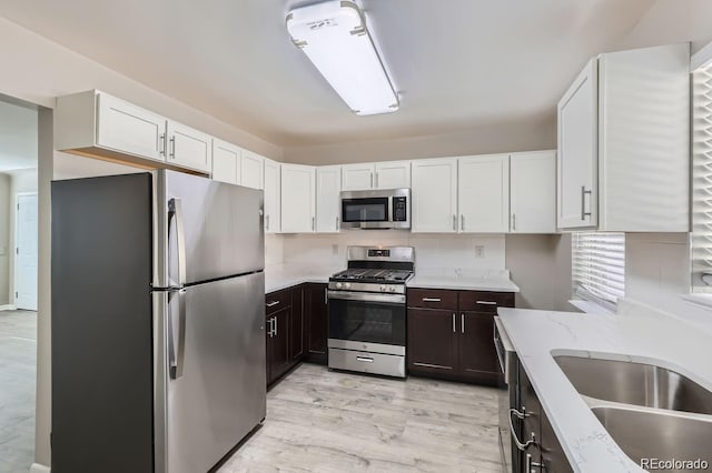 384 S Decatur St, Denver, CO 80219 - kitchen with appliances with stainless steel finishes, white cabinetry, light wood-style floors, and dark brown cabinets