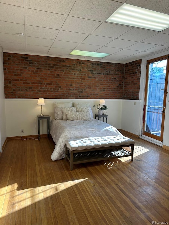 unfurnished bedroom with access to outside, a drop ceiling, and brick wall