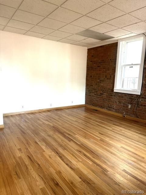 unfurnished room with a paneled ceiling, light hardwood / wood-style flooring, and brick wall