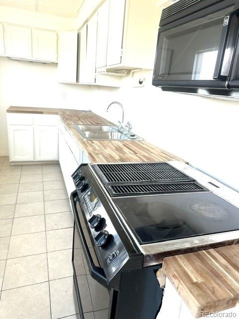 kitchen featuring wooden counters, black appliances, white cabinets, sink, and light tile patterned flooring