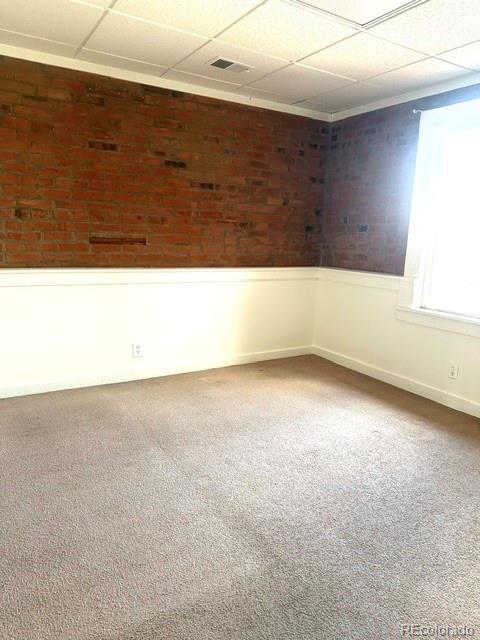 carpeted spare room with a drop ceiling and brick wall