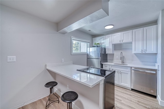 kitchen with sink, stainless steel appliances, a kitchen breakfast bar, light hardwood / wood-style flooring, and white cabinets