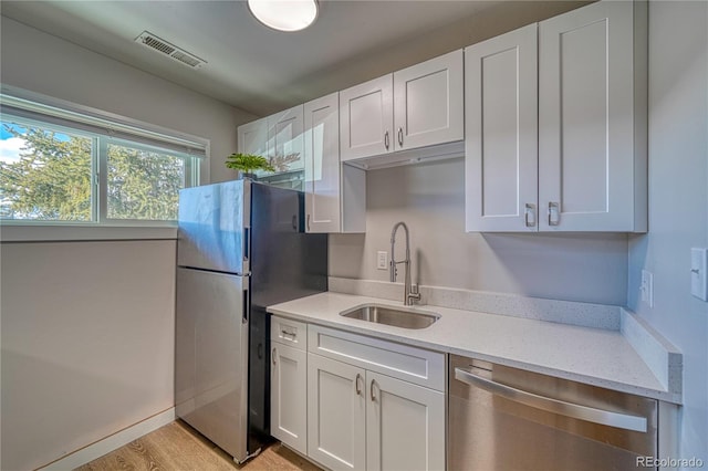 kitchen featuring sink, light hardwood / wood-style flooring, light stone countertops, appliances with stainless steel finishes, and white cabinetry