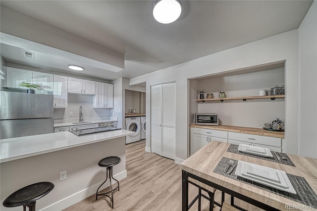 kitchen with sink, stainless steel fridge, light hardwood / wood-style floors, white cabinets, and washer and dryer