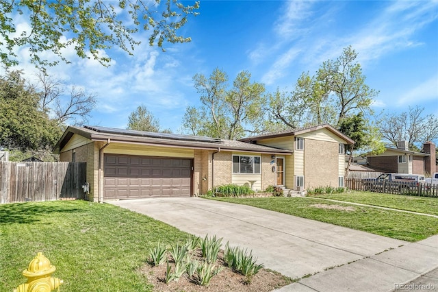 split level home with brick siding, an attached garage, roof mounted solar panels, and concrete driveway