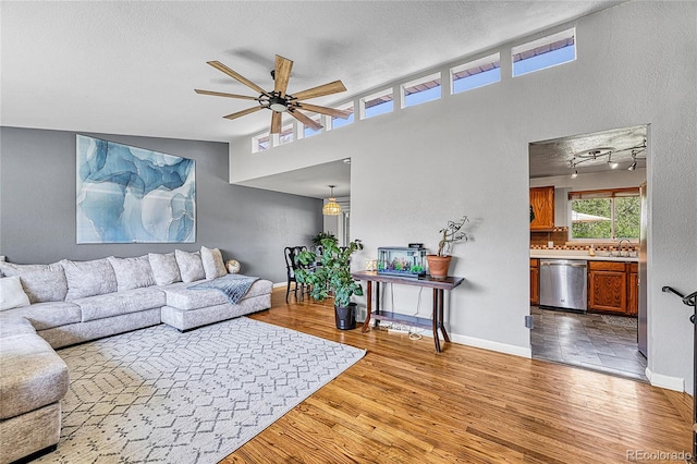 living room with wood finished floors, a ceiling fan, baseboards, and a textured ceiling