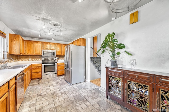 kitchen with stainless steel appliances, a sink, track lighting, light countertops, and decorative backsplash
