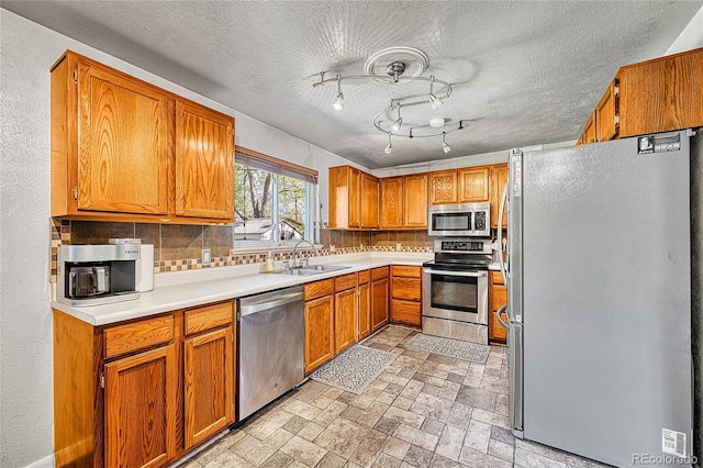 kitchen with stainless steel appliances, a sink, decorative backsplash, light countertops, and a textured ceiling