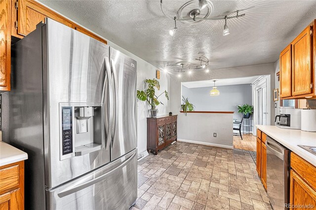 kitchen featuring stainless steel appliances, light countertops, brown cabinetry, baseboards, and a textured ceiling