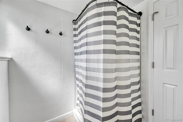 bathroom with a textured wall, a shower with shower curtain, and baseboards