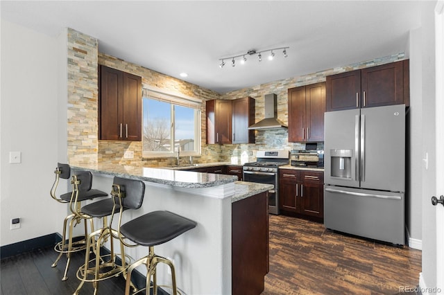 kitchen with kitchen peninsula, dark hardwood / wood-style flooring, wall chimney exhaust hood, appliances with stainless steel finishes, and a breakfast bar area