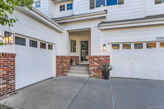 doorway to property featuring brick siding, a garage, and concrete driveway